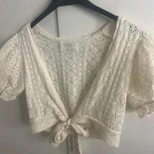 Vit stickad topp från Zara - En fin vit stickad topp från Zara med korta puffärmar i spets och knytning framtill. Perfekt till sommaren.