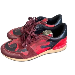 Valentino sneakers i rött och svart - Snygga Valentino sneakers i en djärv röd och svart färgkombination med mönster. Skorna har snörning och en bekväm sula. Perfekta för att ge din outfit en lyxig touch.