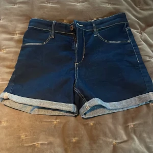 Mörkblå jeansshorts från &Denim - Snygga mörkblå jeansshorts från &Denim med uppvikta ben och kontrastsömmar. Perfekta för en avslappnad stil. De har en klassisk femficksdesign och stängs med knapp och dragkedja framtill.