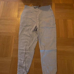 Randiga byxor från Just Junkies - Snygga randiga byxor från Just Junkies i en ljus färg med smala ränder. Byxorna har en elastisk midja med snörning för extra komfort. Perfekta för en avslappnad stil.