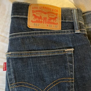 Levis 511 jeans - Snygga Levis 511 jeans i mörkblå denim. De har en klassisk femficksdesign och en dragkedja. Perfekta för en stilren look. Sitter slimfit.