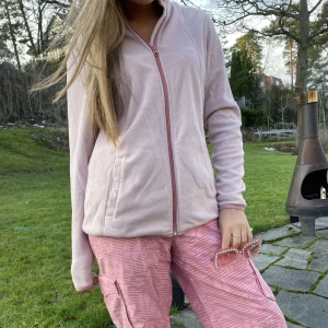 Rosa fleecejacka med dragkedja - Mysig rosa fleecejacka med dragkedja framtill. Perfekt för afterski med sin mjuka och bekväma passform. Jackan har långa ärmar och en enkel design som gör den lätt att matcha med olika outfits