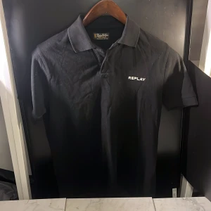 Svart pikétröja från Replay - Snygg svart pikétröja från Replay med klassisk krage och korta ärmar. Perfekt för en stilren look. Märkeslogga på bröstet ger en extra touch. Hör av er vid minsta fundering🙌