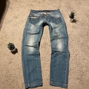 Blå jeans från Miss Sixty - Snygga blå jeans från Miss Sixty med en klassisk femficksdesign och slitna detaljer. De har en knappgylf och är tillverkade i Italien. Perfekta för en avslappnad stil.