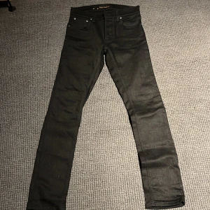 Svarta jeans från Nudie Jeans - Snygga svarta jeans från Nudie Jeans med en klassisk femficksdesign. De har en knappgylf och är tillverkade i ett slitstarkt denimtyg. Perfekta för en stilren look.