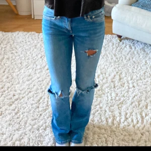 Blå jeans med slitningar - Snygga blå jeans med slitningar på knäna och en klassisk femficksdesign. De har en Bootcut passform och är perfekta för en avslappnad stil. Jeansen har en knappgylf och är tillverkade i ett bekvämt denimtyg.