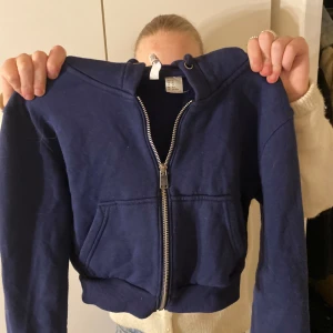 Mörkblå hoodie med dragkedja - Säljer en mörkblå ”croppad”  hoodie med dragkedja och fickor framtill.