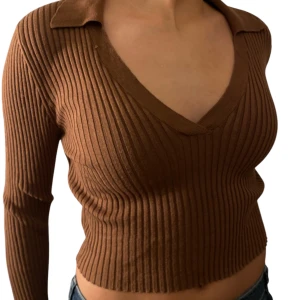 Brun ribbad tröja - Säljer en snygg brun ribbad tröja med v-ringning och krage. Tröjan är croppad och har långa ärmar, perfekt för en trendig look. Passar bra till jeans eller kjol.