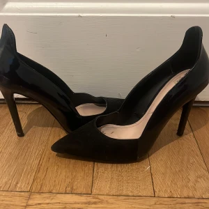 Svarta pumps från Zara - Eleganta svarta pumps från Zara med spetsig tå och hög klack. Skorna har en glansig finish som ger en stilren look. Perfekta för att lyfta vilken outfit som helst.