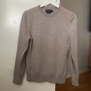 Beige tröja i merinoull från Riley - Säljer en stilren beige tröja från Riley i mjuk merinoull. Tröjan har en klassisk rund hals och långa ärmar, perfekt för alla dagar. Den är enkel att matcha med olika outfits och ger en elegant touch. Den är i mycket bra skick. Den är i storlek S men sitter som XS.