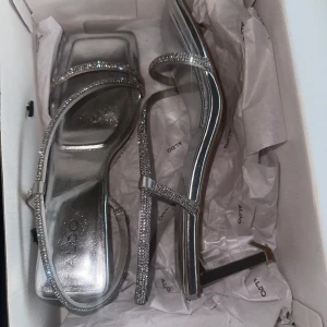 Glittriga silver sandaler från Aldo - Snygga glittriga sandaler i silver från Aldo med smala remmar och klack. Perfekta för att ge en touch av glamour till din outfit. Sandalerna har en fyrkantig tå och en elegant design. (Säljs pågrund av att dom passade inte) (har aldrig kommit till användning) 💕💕💕