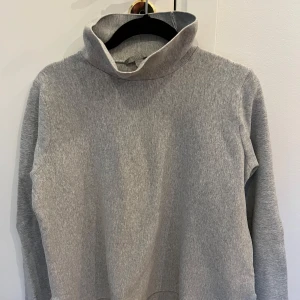 Grå polotröja från COS - Säljer en stilren grå polotröja från COS. Tröjan har en klassisk design med långa ärmar och en bekväm polokrage. Perfekt för kyligare dagar och enkel att matcha med olika outfits.