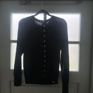 Svart kofta med knappar - Elegant svart kofta med långa ärmar och dekorativa knappar framtill. Perfekt för en stilren look.