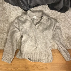 Beige tröja från H&M - Säljer en stilren grå tröja från H&M i storlek xs/s. Tröjan har en klassisk krage och långa ärmar med ribbade muddar. Perfekt för kyligare dagar.