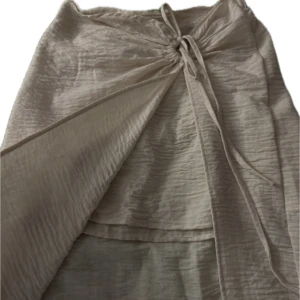 Gräddvit linnekjol med knyt och slit - Snygg, beige, lång omlottkjol med knyt framtill. Kjolen har en elegant och luftig design, perfekt för varmare dagar. Den har ett högt slit och underkjol i samma material. Den är tillverkad i ett lätt och bekvämt material.