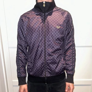 Rutig tröja från Fred Perry - Snygg rutig jacka från Fred Perry i mörka nyanser. Jackan har en dragkedja framtill och långa ärmar med ribbade muddar. Perfekt för en stilren look.