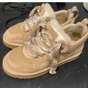 UGG lowmel sneakers - Säljer ett par beige sneakers från UGG med mysigt foder och tjocka snören i vitt och beige. Skorna har en robust sula och är perfekta för kyligare dagar. De är både stiliga och bekväma. Det kommer med extra snören skriv för bild💗