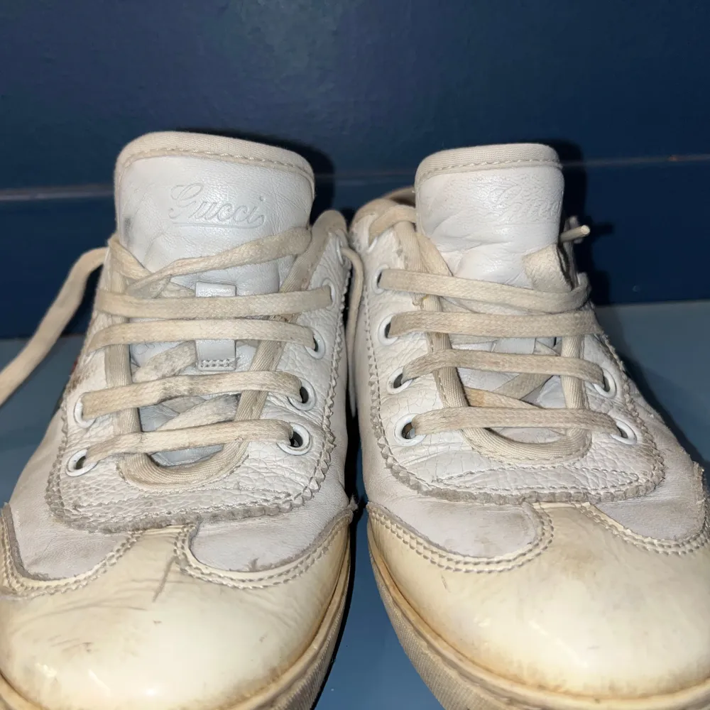 Snygga beige sneakers från Gucci med klassiska ränder i grönt och rött på sidan. Skorna har snörning och är tillverkade i skinn. Perfekta för en stilren look.lite smutsiga men väldigt snygga.. Kengät.