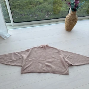 Beige/rosa stickad tröja - Säljer en mysig beige/lite åt det rosa hållet, stickad tröja med långa ärmar. Perfekt för kyligare dagar och ger en avslappnad look. Tröjan har en enkel design med ribbade kanter vid ärmslut och nederkant. Lite kortare modell.