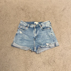 Blå jeansshorts från H&M - Säljer ett par snygga blå jeansshorts från H&M i storlek M. Shortsen har en cool slitning och uppvikta kanter för en avslappnad look. Perfekta för sommardagar! 🩳