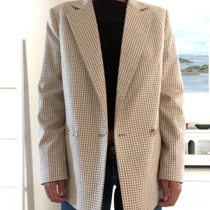 Brun/beige rutig kavaj - Säljer en brunrutig kavaj i storlek S. Kavajen har en oversize passform med dubbelknäppning framtill och långa ärmar. Den är perfekt för både vardag och fest och ger en stilren look. Materialet känns bekvämt och är av hög kvalitet. 