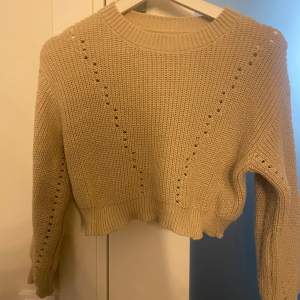 Säljer en superfin beige stickad tröja. Den är croppad och har ett snyggt mönster med små hål längs ärmarna och fram. Perfekt för höst och vinter! Tröjan är i nyskick och väldigt mysig att ha på sig. Passar perfekt till både jeans och kjol.