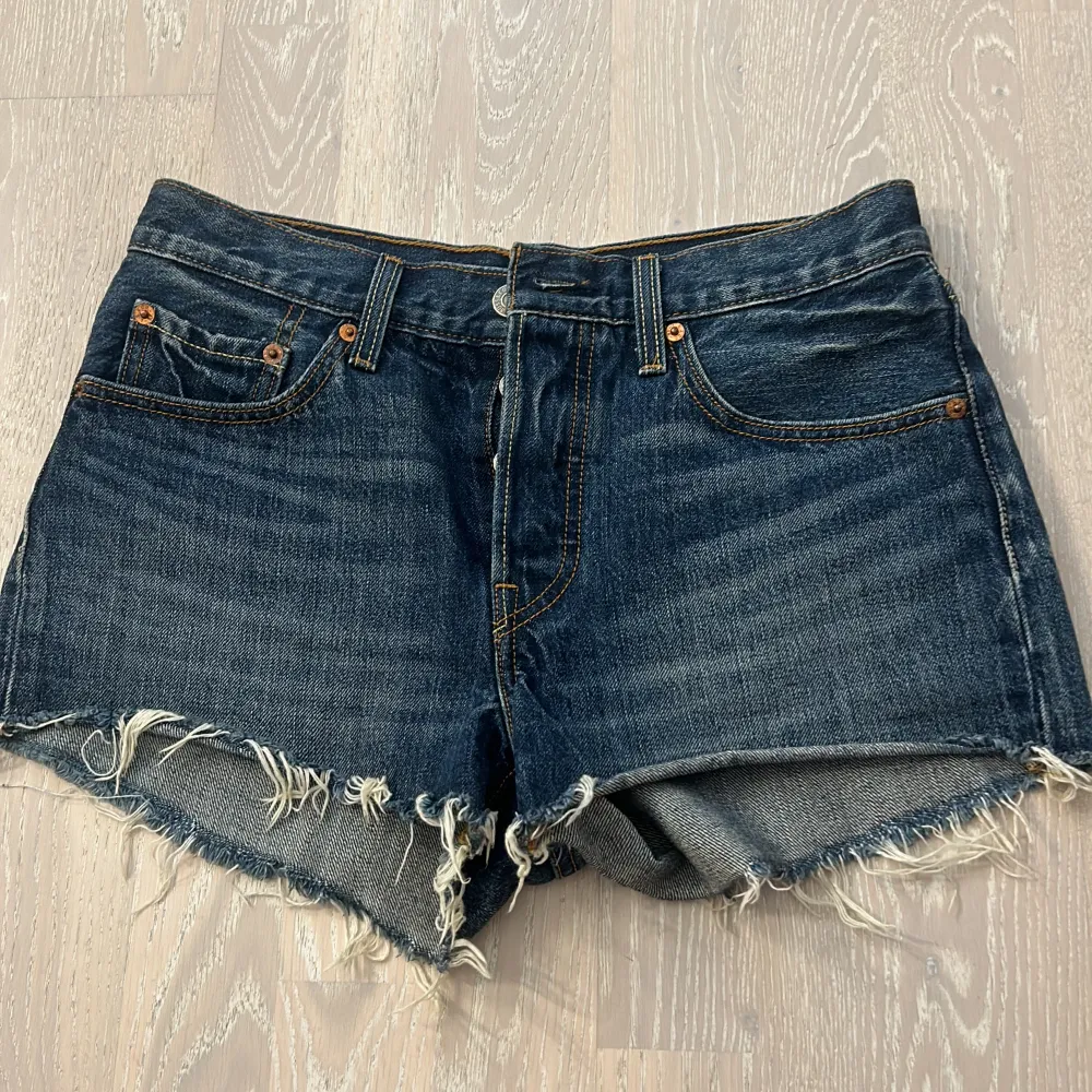 Säljer ett par snygga jeansshorts från Levi's. De är mörkblå och har en rå kant nertill som ger en cool, avslappnad look. Shortsen har knappar istället för dragkedja och klassiska fem fickor. Perfekta för sommaren!. Shorts.