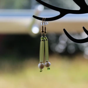 Gröna örhängen med pärlor - Säljer ett par snygga gröna örhängen med pärlor. De har en unik design med två gröna stavar och små pärlor i olika nyanser av grönt och vitt. Perfekta för att ge en färgklick till din outfit!