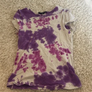 Lila och vit batik t-shirt från H&M - Säljer en cool tie-dye t-shirt från H&M i storlek S. T-shirten är vit med lila och rosa mönster och har korta ärmar. Perfekt för en avslappnad och trendig look! 💜
