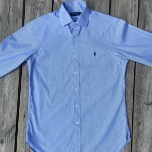 Vit och Ljusblå randig Ralph Lauren skjorta - Säljer denna riktigt stiliga vit- och ljusblårandiga skjorta från Ralph Lauren för 549kr. Skjortan hat inga hål, fläckar eller andra defekter. Modellen på bilden är 181cm lång.