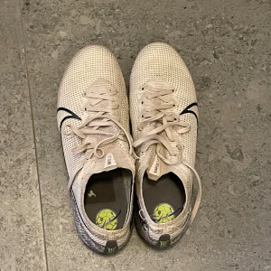 Nike Mercurial Vapor 13 Elite FG - Säljer dessa riktigt snygga och bra fotbollskor. De är relativt använda men är i bra skick. De fungerar på gräs och konstgräs och de har färgen ”Dessert Sand”. Storlek är 39. Skick 8/10. Tillhörande påse följer med. Priset kan förhandlas