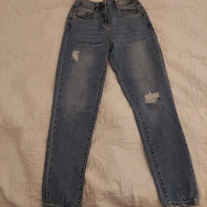 Blå jeans med slitningar - Säljer ett par snygga blå jeans med coola slitningar på låren. Aldrig använd, råkade köpa fel storlek och gick inte att lämna tillbaka. Annars så fin.