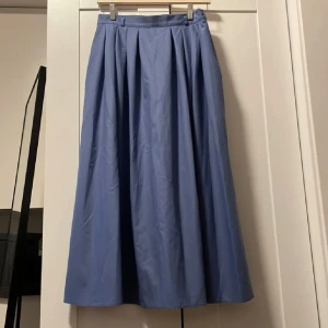 Blå långkjol - Säljer en superfin blå långkjol i ett klassiskt snitt. Kjolen har en elegant och flytande design med veckade detaljer som ger den extra volym. Perfekt för både vardag och festliga tillfällen. Den är i bra skick och redo för en ny garderob!