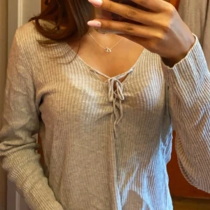 Beige ribbad tröja från Bik Bok - Säljer en superfin grå ribbad tröja från Bik Bok. Den har en snygg v-ringning med snörning framtill som ger en extra detalj. Tröjan är långärmad och perfekt för både vardag och fest. Super fint skick. Stl L men passar även M och S 