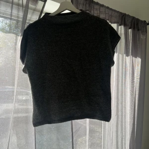 Grå stickad tröja - Säljer en mysig grå stickad tröja. Perfekt för kyliga dagar med sin mjuka och bekväma passform. Tröjan har korta ärmar och en enkel design som gör den lätt att matcha med olika outfits.