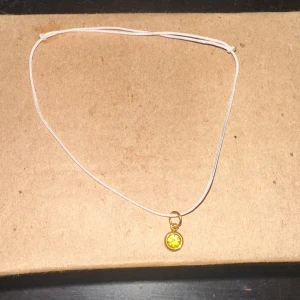 Vitt armband med gul hängsmycke - Säljer ett enkelt och stilrent vitt armband med ett litet runt gult hängsmycke. Perfekt för att lägga till en subtil färgklick till din outfit. Passar både till vardags och fest!