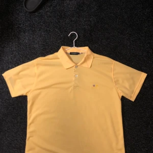 Gul pikétröja från Burberry - Säljer en snygg gul pikétröja från Burberry. Den har en klassisk krage med knappar och det ikoniska Burberry-märket broderat på bröstet. Perfekt för en stilren och avslappnad look. Passar både till vardags och fest!  