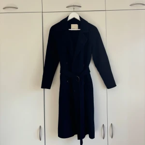 Mörkblå kappa från Levete - Lite tunnare mörkblå kappa med knappar samt bälte i midjan. Väldigt fint material.   