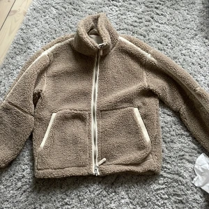 Beige teddyjacka från H&M - Säljer en supermysig beige teddyjacka från H&M. Den har en dragkedja framtill och stora fickor som är perfekta för att värma händerna i. Jackan är långärmad och gjord i ett mjukt teddy-material som är perfekt för kyliga höst- och vinterdagar. Den är i storlek S och passar perfekt för en avslappnad och bekväm stil.
