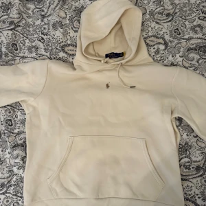 Beige hoodie från Ralph Lauren - Säljer en snygg och stilren beige hoodie från Ralph Lauren. Den har en klassisk design med en liten broderad logga på bröstet och en praktisk magficka. Perfekt för en avslappnad och trendig look!