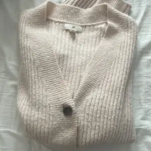 Säljer en supermysig beige kofta från H&M. Den är ribbad och har en v-ringad design med stora knappar framtill. Perfekt för höst och vinter. Koftan har långa ärmar och är i ett bra skick