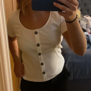 Vit ribbad topp med knappar - Superfin vit ribbad topp från aware (Vero Moda). Den har korta ärmar och en rad med snygga knappar framtill. Stor i storlek för att vara en xs💓💓