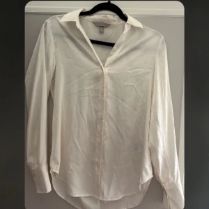 Vit blus med krage - Säljer en stilren och klassisk vit blus med krage. Den har långa ärmar och är perfekt för både vardag och fest. Materialet som är satin känns lätt och luftigt, vilket gör den bekväm att bära hela dagen.