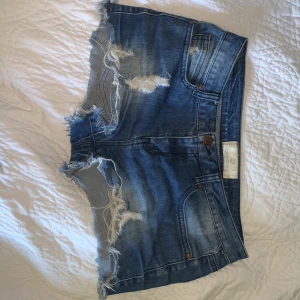 Blå jeansshorts från Guess - Säljer ett par snygga blåa lågmidjade jeansshorts från pieces. De har en cool distressed look med slitna detaljer och fransiga kanter. Perfekta för en avslappnad sommarstil! 🕶️skriv för fler bilder❤️