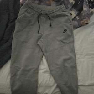 Grey Nike Sportswear Tech Fleece Pants - Grå nike tech byxor i storlek M, använda ett flertal gånger. Ena snöret är förstört, annars inga problem med byxorna👍🏽 Vill bli av med dom så snabbt som möjligt och just för att snöret är förstört så säljs byxorna för 150 kr.