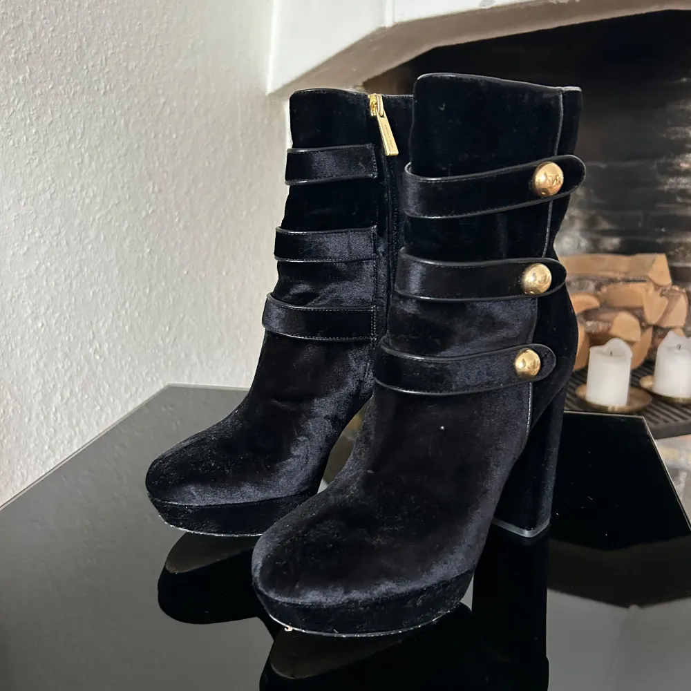 Säljer ett par eleganta svarta boots i sammet från Michael Kors. De har en stilren design med tre dekorativa remmar och guldfärgade knappar. Skorna har en dragkedja på sidan för enkel på- och avtagning. Perfekta för höst och vinter! Andvänt ett få tal gånger. 10cm klack 2cm platå. Skor.