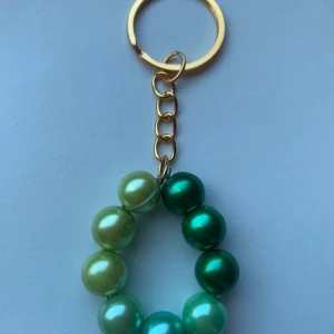 Nyckelring med gröna pärlor - Snygg nyckelring med gröna pärlor i olika nyanser. Pärlorna är trädda på en ring och fästa i en guldfärgad kedja. Perfekt accessoar för att ge dina nycklar lite extra stil!