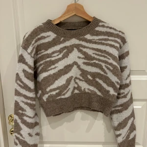 Brun och vit zebramönstrad croppad tröja - Säljer en supercool brun och vit zebramönstrad tröja. Den är croppad och har långa ärmar, perfekt för att ge din outfit en trendig touch. Materialet är mjukt och skönt, perfekt för höst och vinter. Passar både till jeans och kjol!