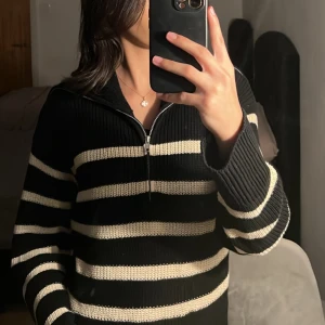 Svart och vit randig stickad tröja - Säljer en supermysig svart och vit randig stickad tröja med dragkedja. Perfekt för kyliga dagar! Den har långa ärmar och en hög krage som kan vikas ner. Tröjan är i nyskick och passar perfekt för både höst och vinter. 🖤🤍