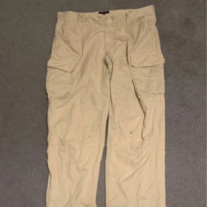 Beige Baggy Cargo Byxor/Slacks - Snygga byxor med baggy/straight fit. Funkar lika bra att klä upp som ner. De är hyfsat använda, lite heel-bites så att säga, men inget större problem. Gylfen är sprucken och jag har sytt igen så gott det går, inte supersnyggt men det syns knappt. 
